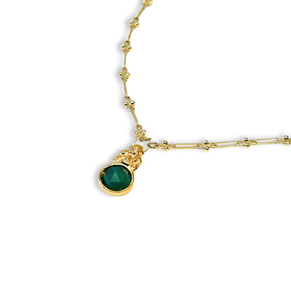 Gold necklace with a green gemstone pendant on a white background